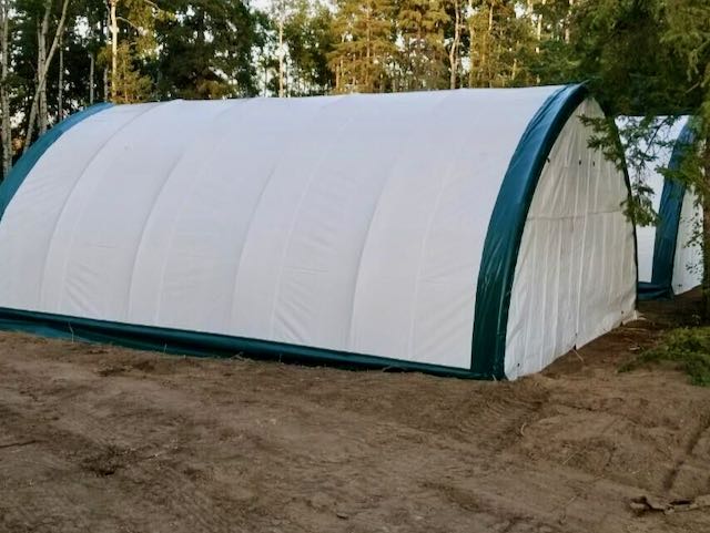 The gold Mountain twenty foot wide by thirty foot long hoop shelter has a white fabric cover with green trim.