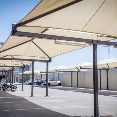 Green apartment parking lot with cantilever shade canopy on metal posts and fabric roof over walkways