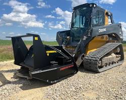 Stinger Mulcher - Cliffhouse Buildings Black forestry disc mulcher attached to a yellow and black skid steer, positioned on gravel with a blue sky and fields in the background.