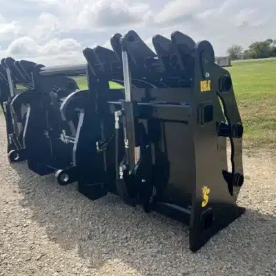 Black 107-inch clam grapple attachment for wheel loaders, featuring robust steel construction, positioned on a gravel path with green grass in the background.