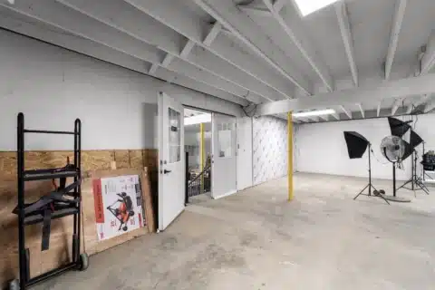 Open lower-level room with support columns and portable lighting equipment.
