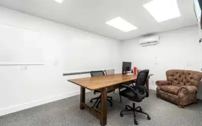 Carpeted office with a large table, chairs and wall-mounted climate unit.