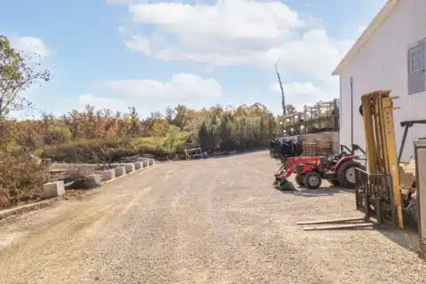 Open gravel work yard behind the building with equipment parked beside it.