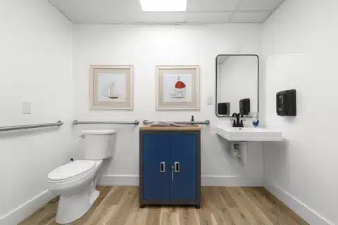 Front view of a larger restroom with grab bars, toilet and wall-mounted sink.