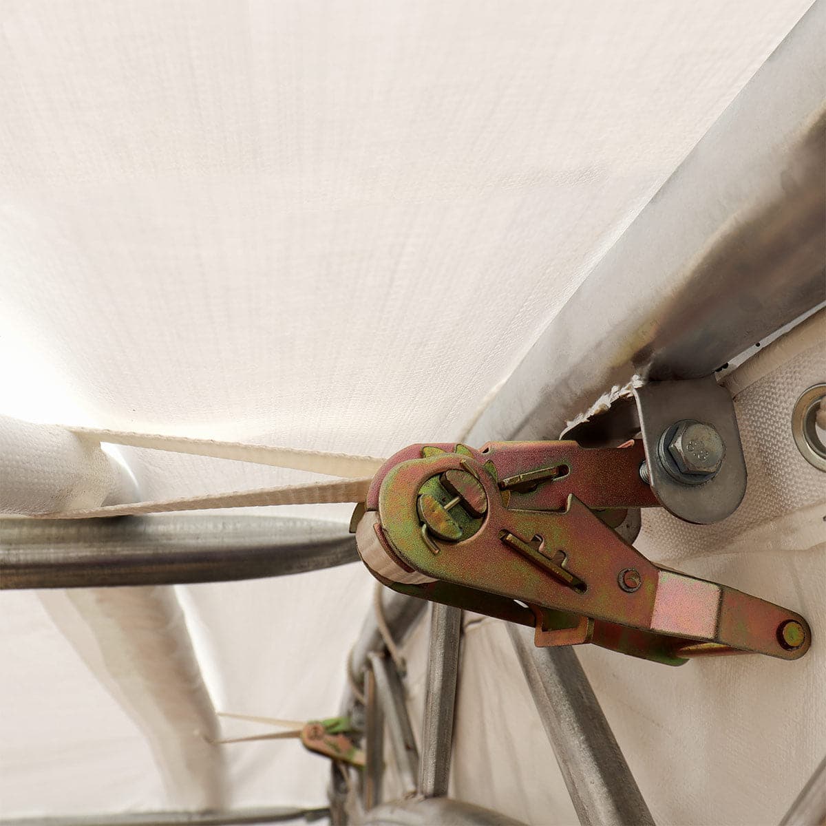 Close-up of metal hinge and strap hardware securing a white fabric canopy to a frame, with a bolt and bracket visible.