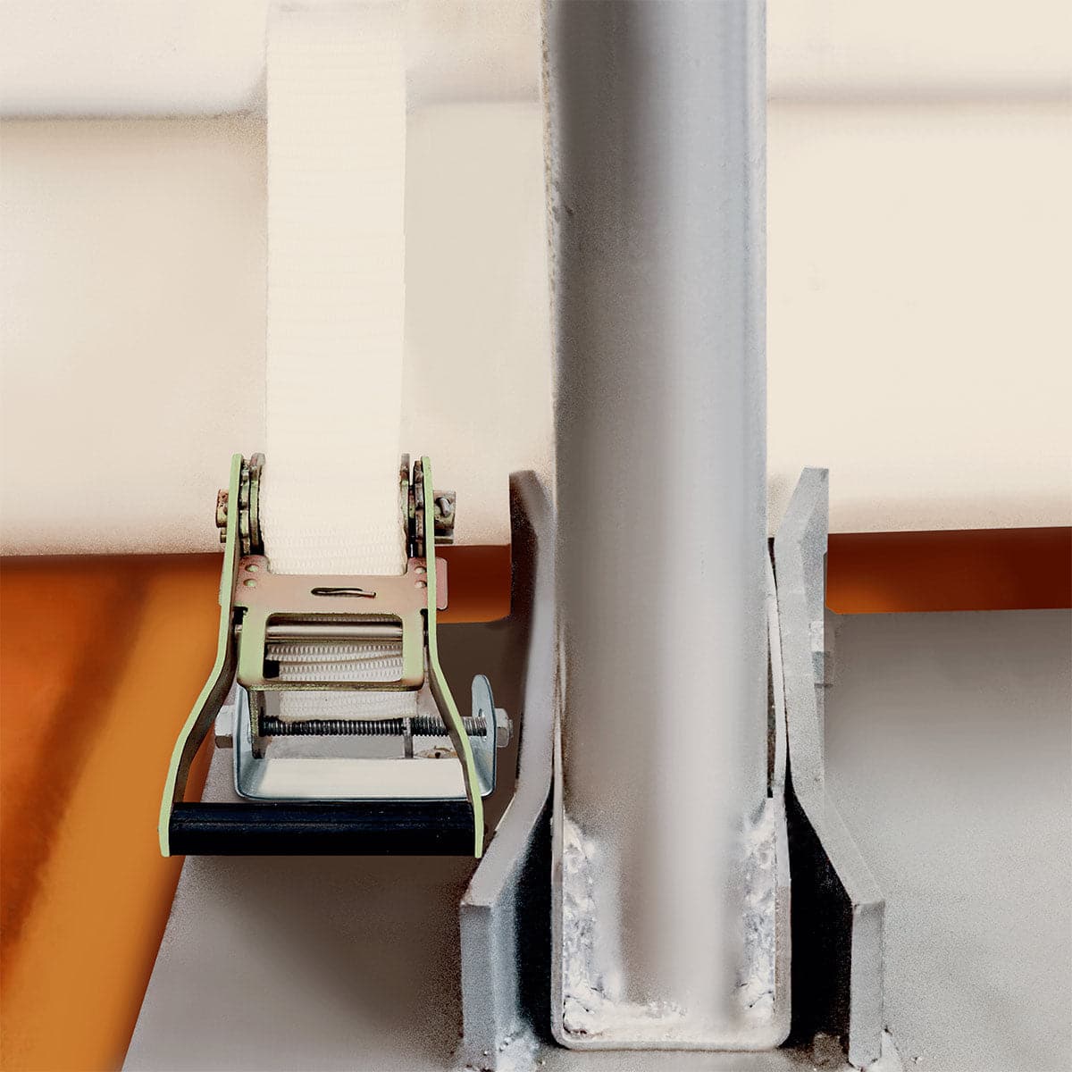 Close-up of a metal strap tensioner gripping a white fabric strap around a vertical steel post, with an orange base surface visible nearby.