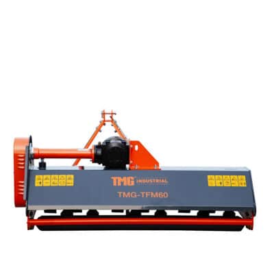 Industrial ground-working attachment with orange frame and gray housing labeled TMG-TFM60, featuring warning decals and a roller beneath for support.