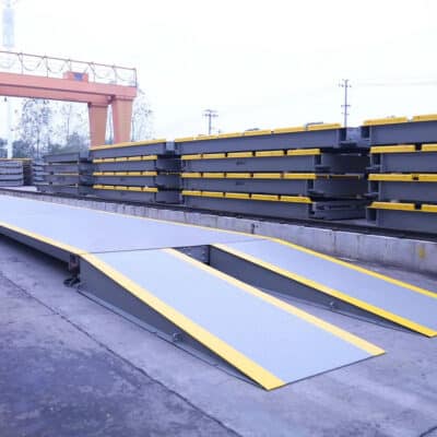 Industrial loading yard with stacked gray steel beams and yellow-edged ramps for forklift access.